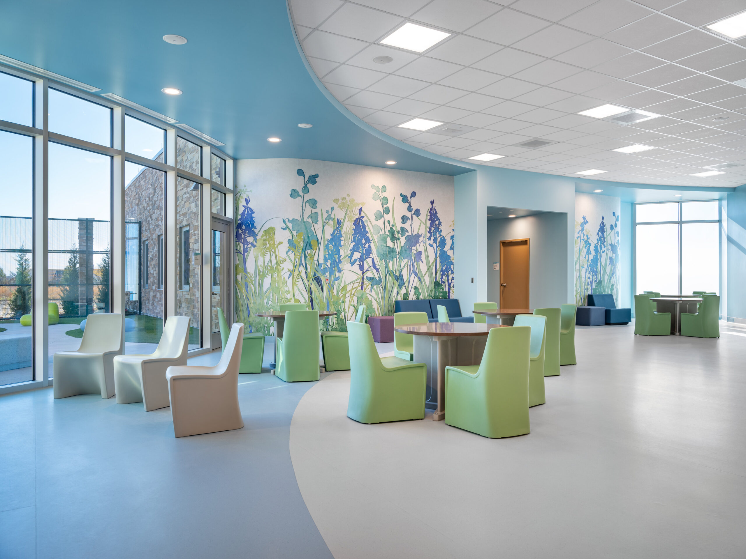 Bright modern lobby with curved turquoise ceiling, large windows, and colorful seating along a floral wall mural in soft blue and green tones.