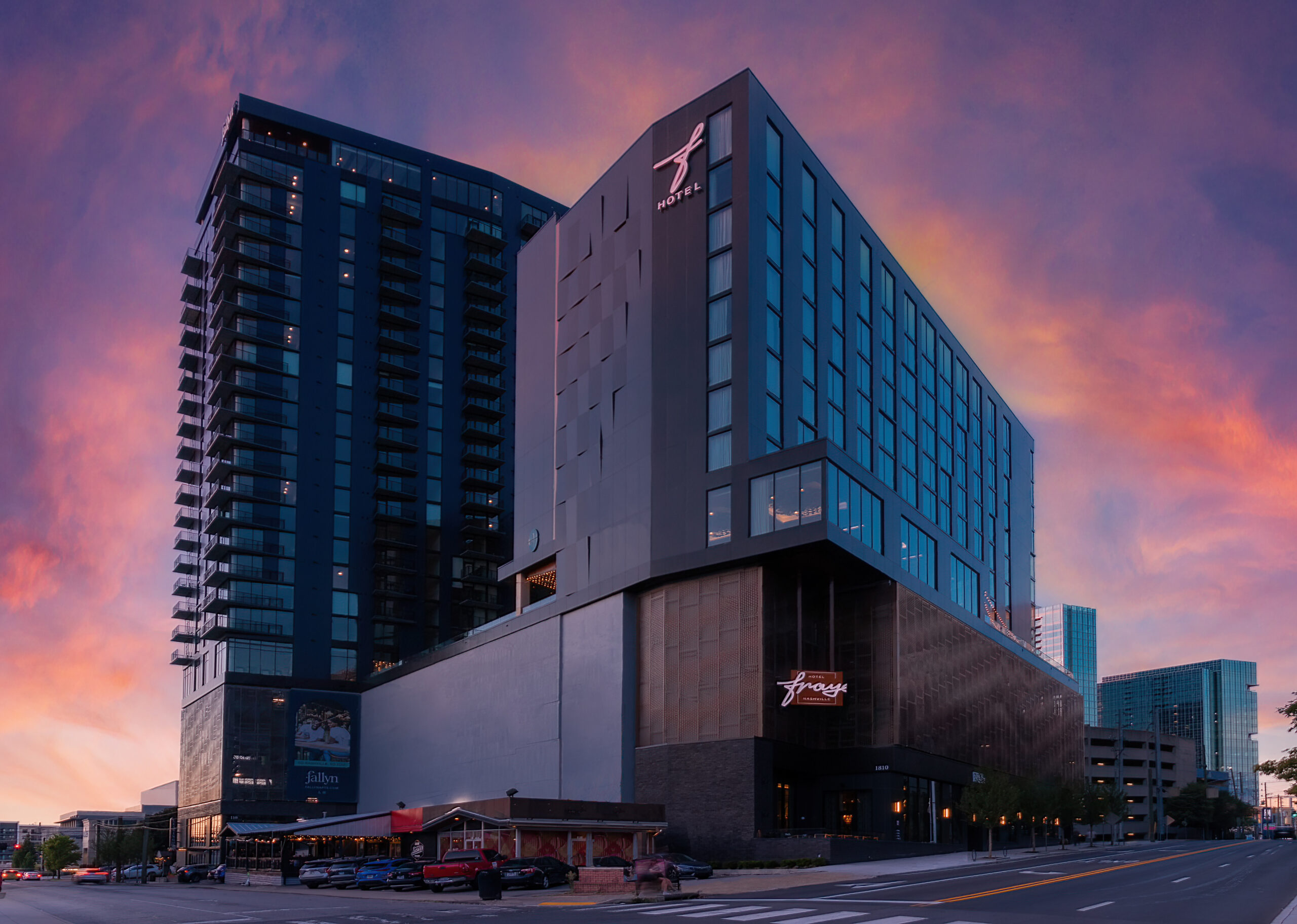 Modern glass hotel building at sunset with a pink-purple sky reflecting off the windows.