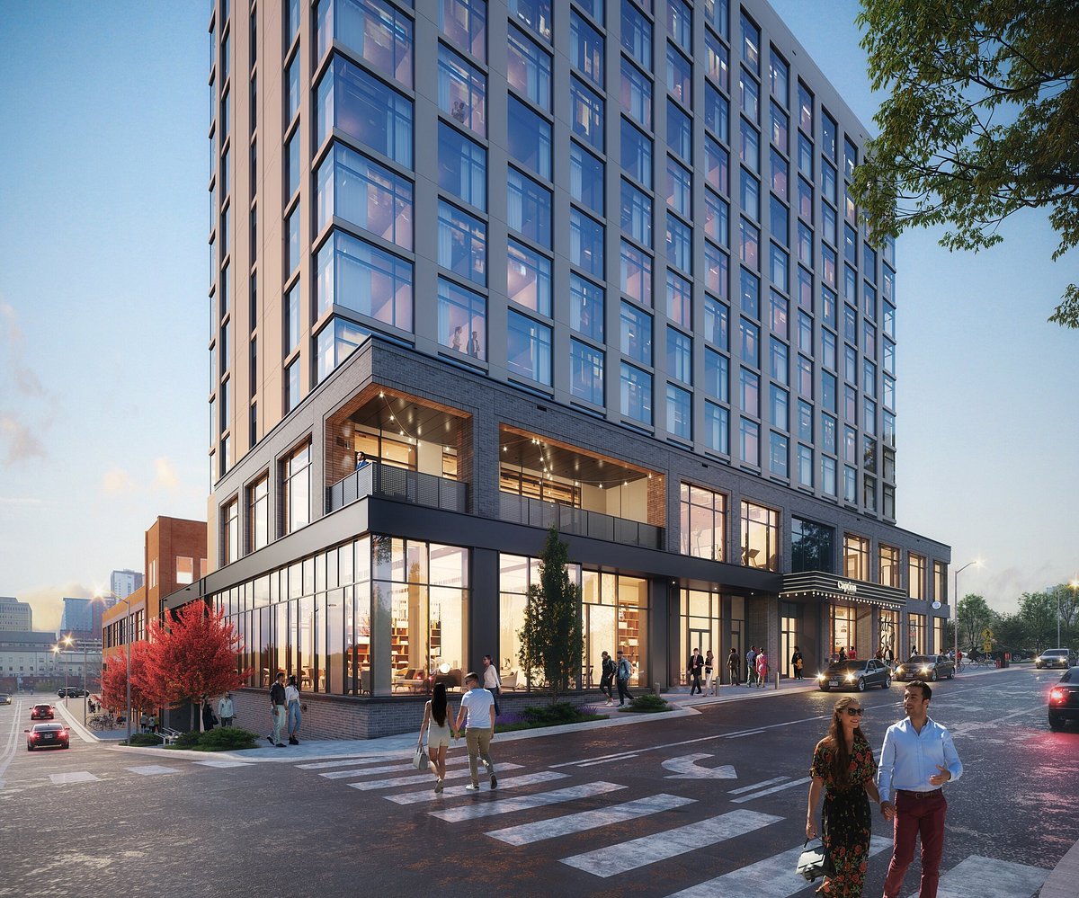 Modern multi-story commercial building with glass storefronts on the ground level and office windows above, on a busy street with pedestrians.