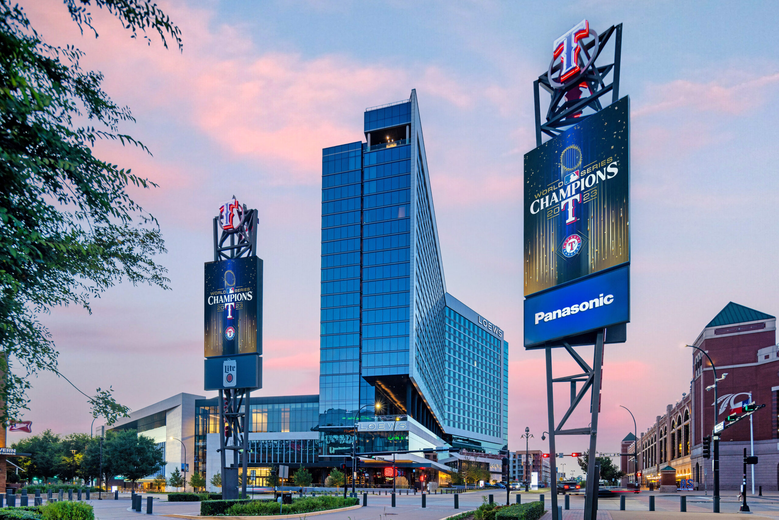 Stadium area with tall electronic signs reading World Series Champions at sunset over a blue-glass building.