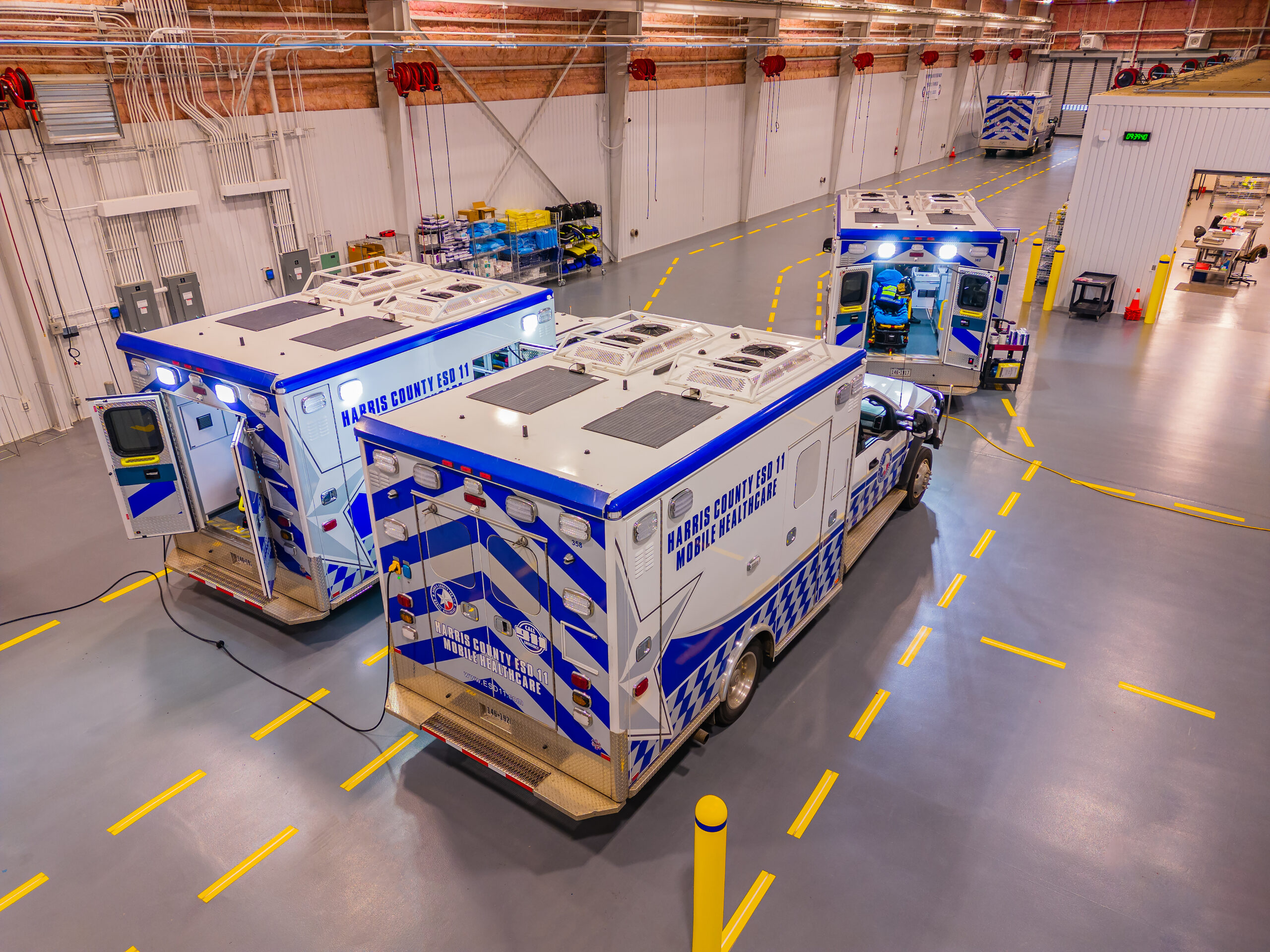 Fleet of blue-and-white EMS ambulances in a spacious hospital garage with yellow floor markings ready for dispatch