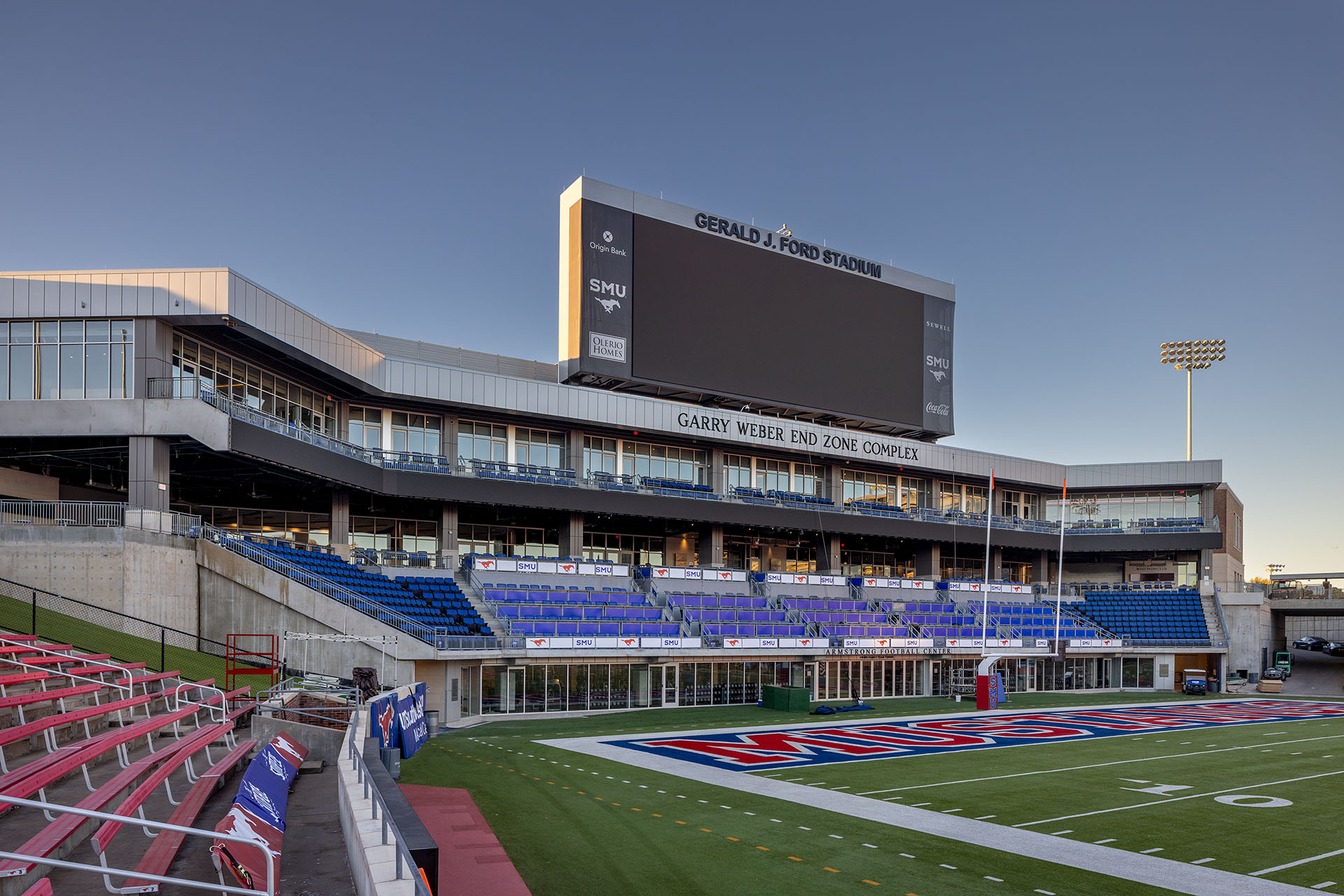 Wide view of Gerald J. Ford Stadium at SMU, featuring a large scoreboard and tiered blue and red seating along the field edge