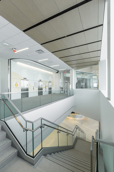 UIHC-109 - Aptitude Interior atrium with a metal-and-glass stairwell descending to a lower level, glass railing and bright overhead lights.